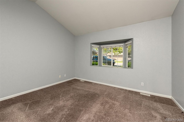 empty room with dark carpet, lofted ceiling, and baseboards
