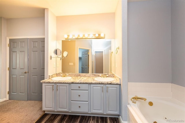 bathroom with a jetted tub, double vanity, and wood finished floors