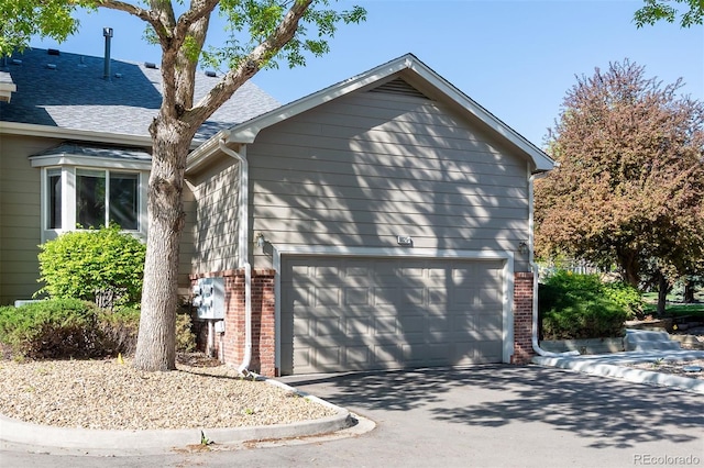 9025 W 79th Way Unit D, Arvada, CO 80005 - view of home's exterior with brick siding, driveway, an attached garage, and roof with shingles
