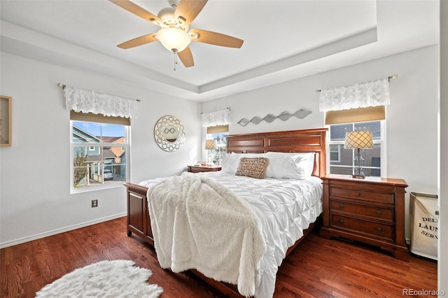 bedroom with ceiling fan, dark wood-type flooring, and a tray ceiling