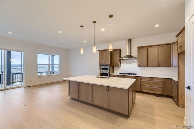231 Leafy Aster Ln, Castle Rock, CO 80104 - kitchen featuring wall chimney exhaust hood, light wood-type flooring, gas cooktop, light stone counters, and a center island with sink