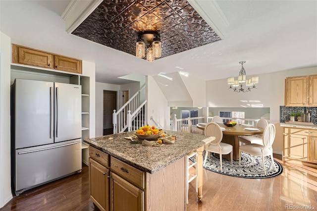 kitchen featuring stainless steel refrigerator, dark wood-type flooring, an inviting chandelier, light stone counters, and backsplash