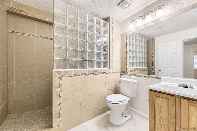 bathroom featuring vanity, tile patterned floors, a textured ceiling, tile walls, and a tile shower