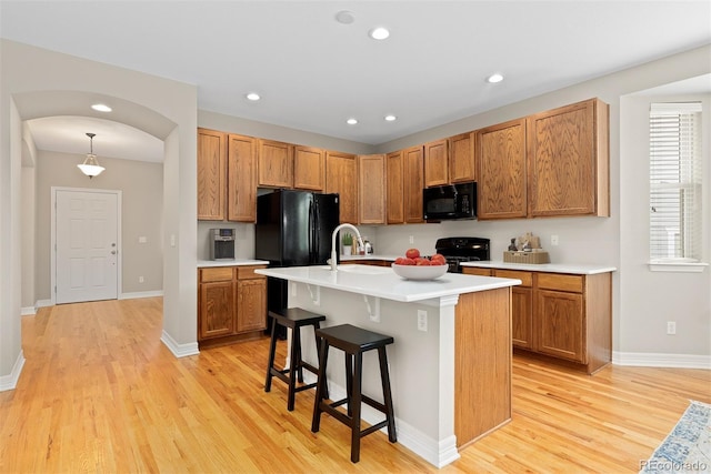 6520 S Newcastle Way, Aurora, CO 80016 - kitchen with black appliances, light wood-type flooring, light countertops, a breakfast bar, and recessed lighting