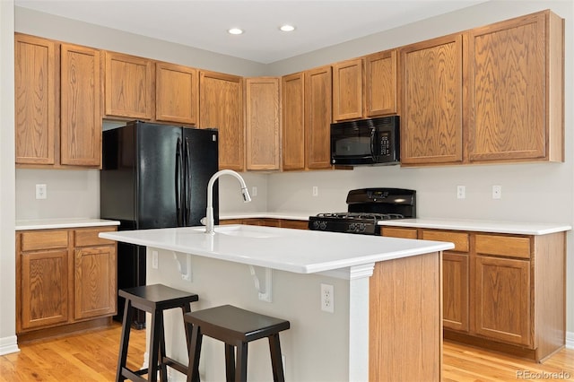 6520 S Newcastle Way, Aurora, CO 80016 - kitchen with black appliances, light wood-type flooring, recessed lighting, a kitchen bar, and an island with sink