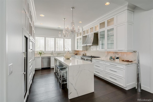 kitchen featuring white cabinets, dishwasher, a center island, wall chimney exhaust hood, and decorative light fixtures