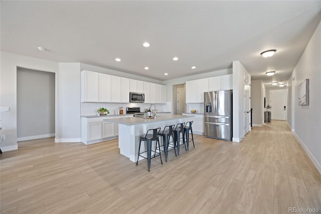 kitchen featuring a kitchen island with sink, baseboards, a kitchen breakfast bar, light wood finished floors, and stainless steel appliances