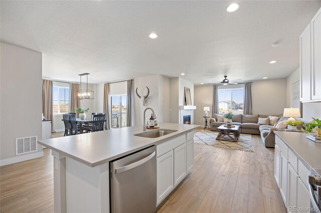 kitchen featuring a warm lit fireplace, a sink, light wood finished floors, stainless steel dishwasher, and visible vents
