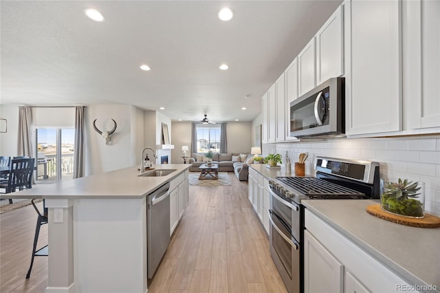 kitchen featuring appliances with stainless steel finishes, a sink, light wood-style floors, recessed lighting, and backsplash