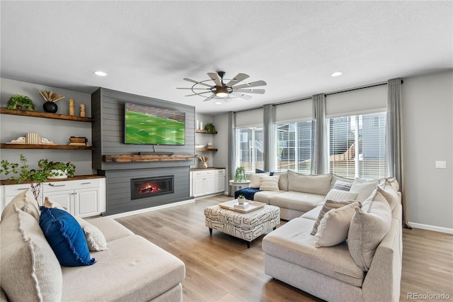 living area with a textured ceiling, recessed lighting, a large fireplace, baseboards, and light wood-style floors