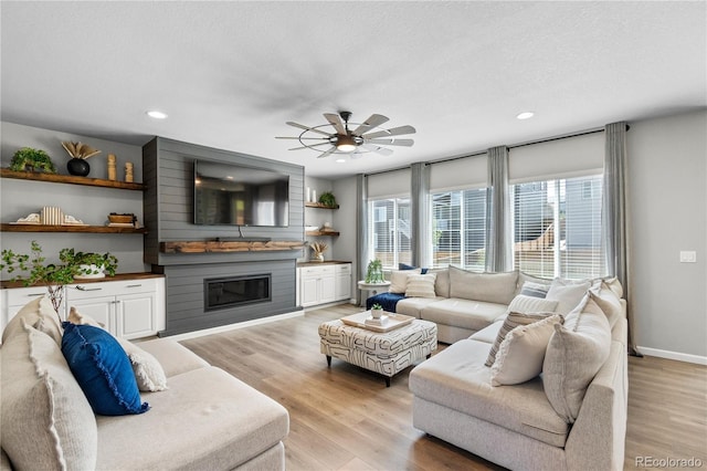 living area featuring a large fireplace, baseboards, a ceiling fan, a textured ceiling, and light wood-style floors