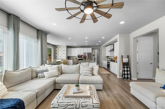 living room featuring ceiling fan, light wood-type flooring, baseboards, and recessed lighting