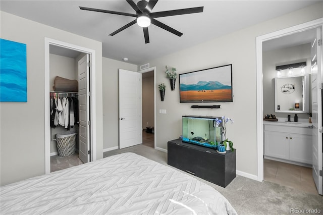 bedroom with a closet, a spacious closet, ensuite bathroom, light carpet, and baseboards