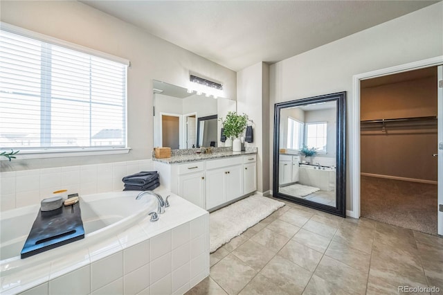 bathroom featuring tile patterned flooring, a garden tub, a spacious closet, and vanity