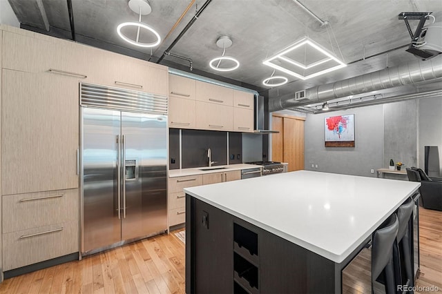 kitchen with stainless steel appliances, sink, a large island, light wood-type flooring, and a breakfast bar