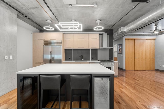 kitchen featuring high quality appliances, light hardwood / wood-style floors, beverage cooler, ceiling fan, and sink