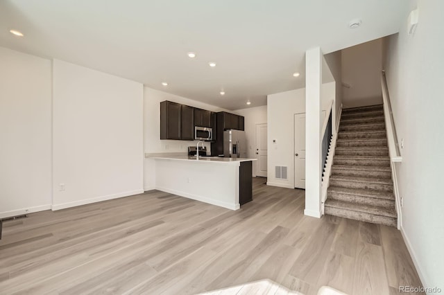 kitchen featuring light wood-style flooring, a sink, stainless steel appliances, a peninsula, and light countertops