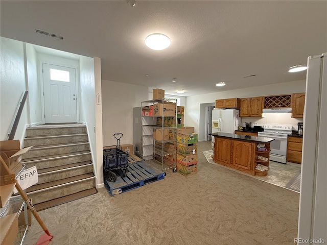 183 E Ave, Limon, CO 80828 - interior space featuring white appliances, dark countertops, brown cabinets, under cabinet range hood, and a kitchen island