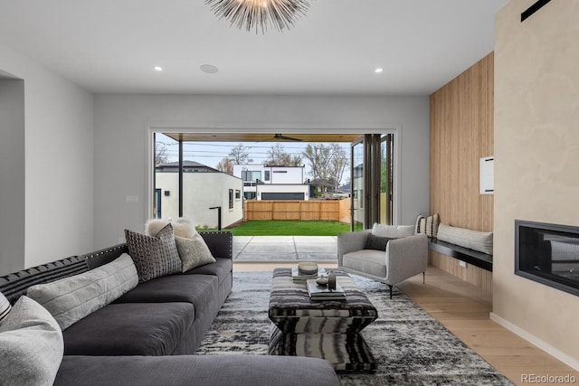 living area with light wood-type flooring, recessed lighting, a glass covered fireplace, and baseboards