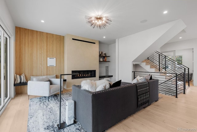 living area with wood finished floors, a glass covered fireplace, stairs, recessed lighting, and wood walls