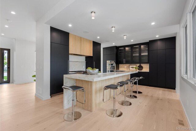 kitchen featuring modern cabinets, dark cabinets, a breakfast bar, light wood finished floors, and recessed lighting