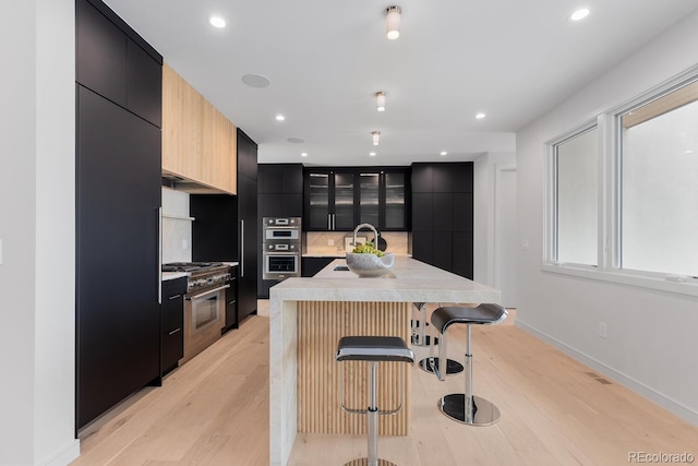 kitchen featuring modern cabinets, dark cabinetry, appliances with stainless steel finishes, a breakfast bar, and light countertops