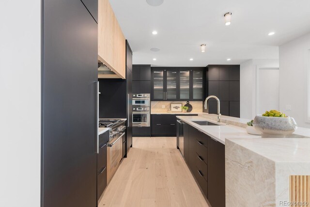 kitchen with modern cabinets, a sink, light wood-type flooring, a large island with sink, and cooktop