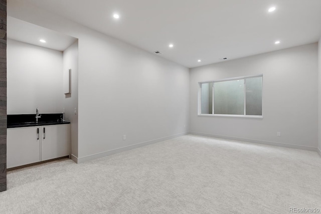 unfurnished living room featuring recessed lighting, light carpet, baseboards, and wet bar