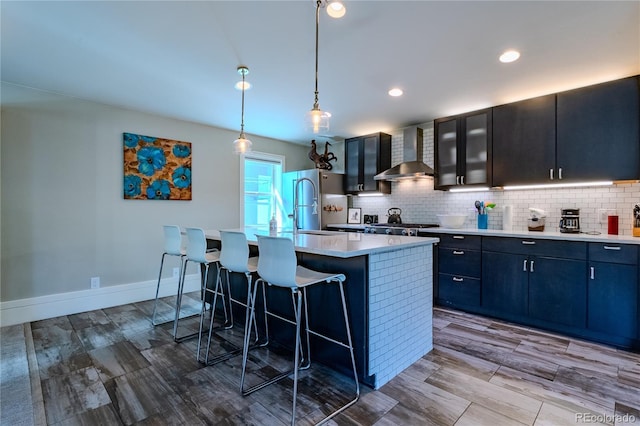 kitchen featuring wall chimney range hood, tasteful backsplash, freestanding refrigerator, a kitchen breakfast bar, and light countertops