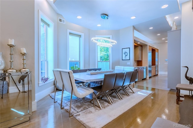 dining room with a chandelier, light wood-type flooring, visible vents, and baseboards