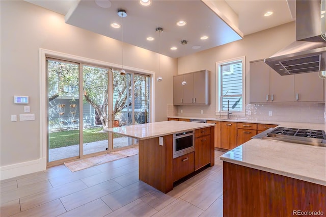 kitchen featuring island exhaust hood, light stone counters, stainless steel gas cooktop, decorative backsplash, and a center island
