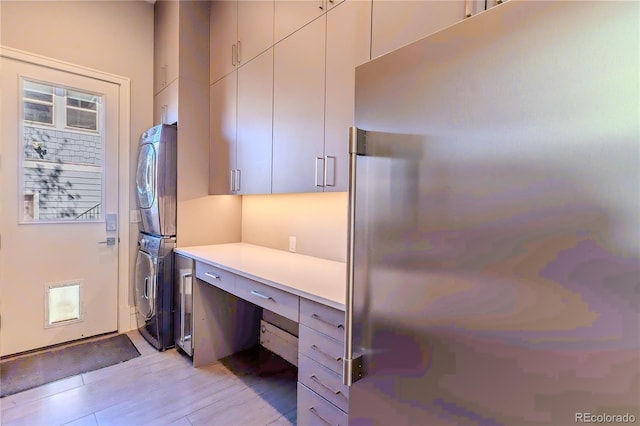 kitchen with built in desk, stainless steel refrigerator, stacked washer / drying machine, light wood-type flooring, and light countertops