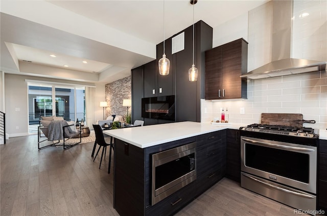 7861 W 51st Ave Unit B, Arvada, CO 80002 - kitchen featuring appliances with stainless steel finishes, wall chimney range hood, a raised ceiling, dark wood-type flooring, and recessed lighting