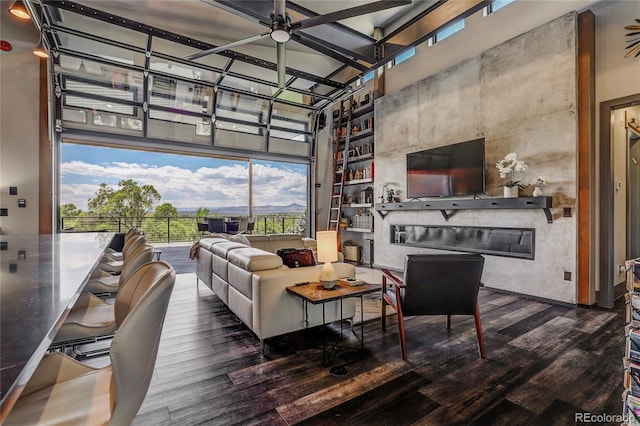 living area featuring a garage, a high ceiling, wood finished floors, and a glass covered fireplace