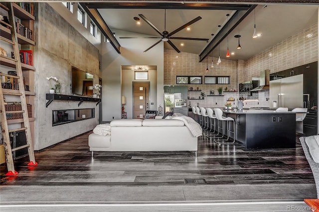 living room featuring a towering ceiling, dark wood-type flooring, and a glass covered fireplace