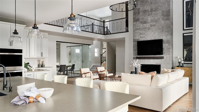 living room with a large fireplace, sink, a high ceiling, a chandelier, and light hardwood / wood-style floors