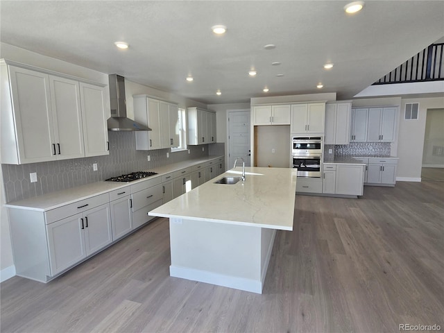 kitchen with a center island with sink, white cabinetry, light wood-type flooring, and wall chimney range hood