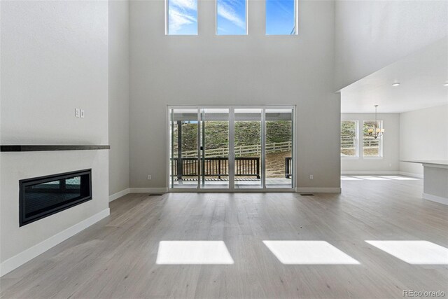 unfurnished living room featuring an inviting chandelier, wood finished floors, a high ceiling, and a glass covered fireplace
