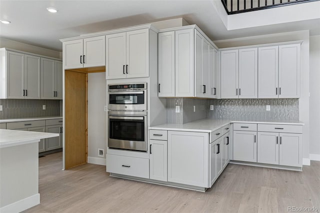 kitchen featuring stainless steel double oven, recessed lighting, light countertops, decorative backsplash, and light wood-style floors