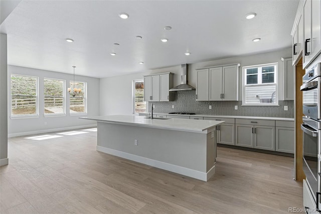 kitchen with light wood-style flooring, a sink, gas cooktop, wall chimney exhaust hood, and backsplash
