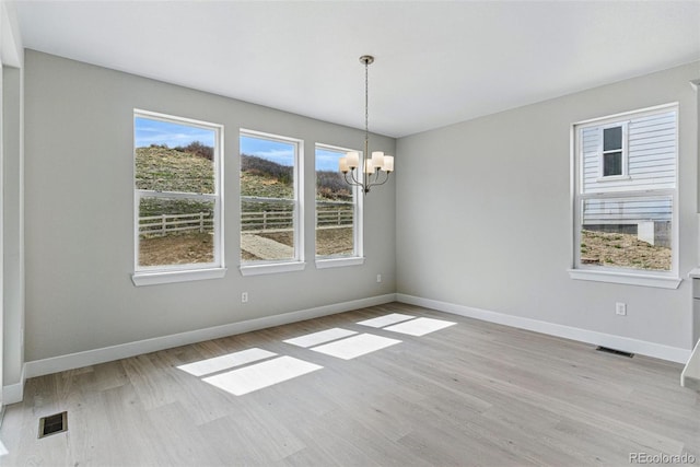 empty room featuring an inviting chandelier, baseboards, visible vents, and light wood-style floors