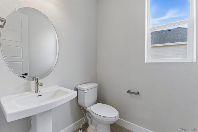 half bathroom with toilet, baseboards, and a sink