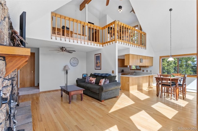 living area featuring baseboards, a baseboard heating unit, a ceiling fan, beamed ceiling, and light wood finished floors