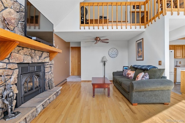 living room with baseboards, a baseboard radiator, ceiling fan, a stone fireplace, and light wood-style flooring