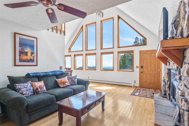living room featuring a stone fireplace, light wood-type flooring, a ceiling fan, a textured ceiling, and baseboard heating