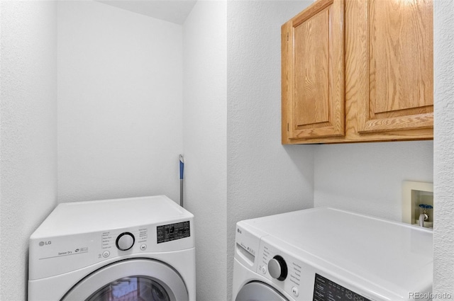 laundry area with a textured wall, independent washer and dryer, and cabinet space