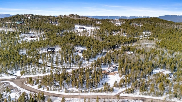 snowy aerial view featuring a wooded view and a mountain view