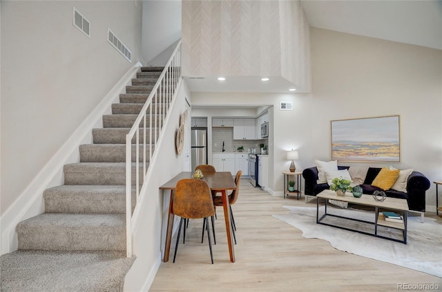 staircase with a towering ceiling, wood finished floors, and visible vents