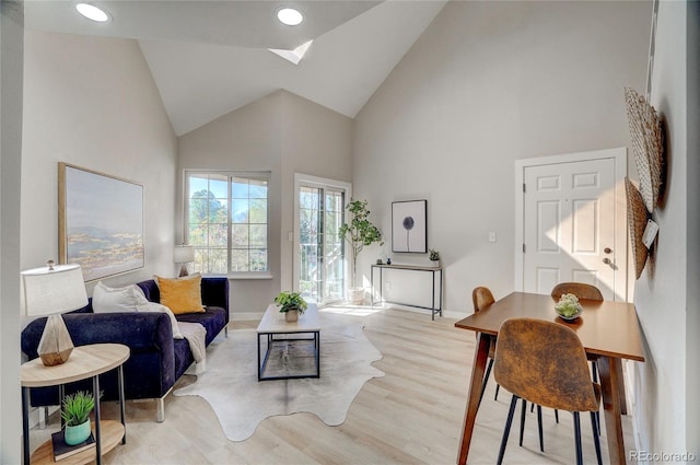 living room with high vaulted ceiling, recessed lighting, a skylight, wood finished floors, and baseboards