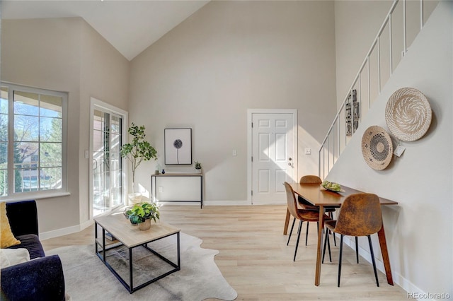 living area featuring high vaulted ceiling, stairway, light wood-type flooring, and baseboards